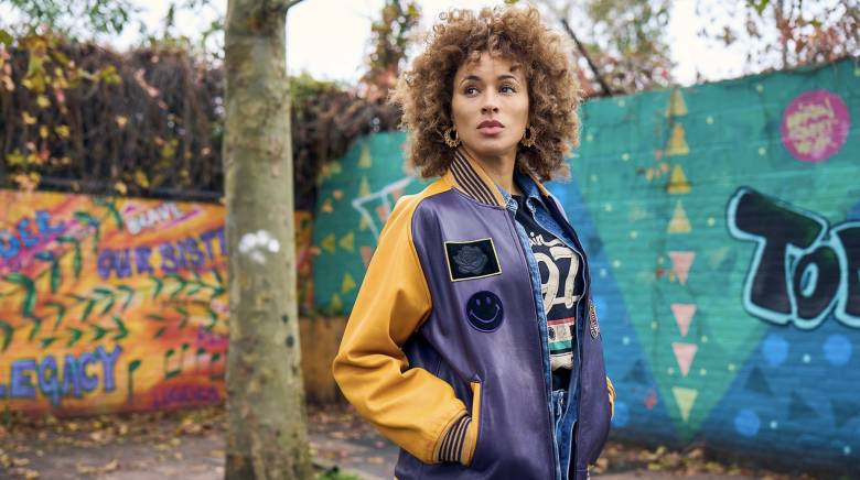 Mia (Michelle De Swarte) stands in front of two walls covered in colourful graffiti.