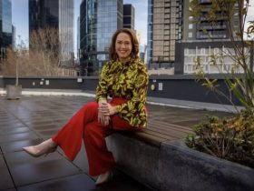 Lisa Millar sitting down on a stone wall outside some offices.