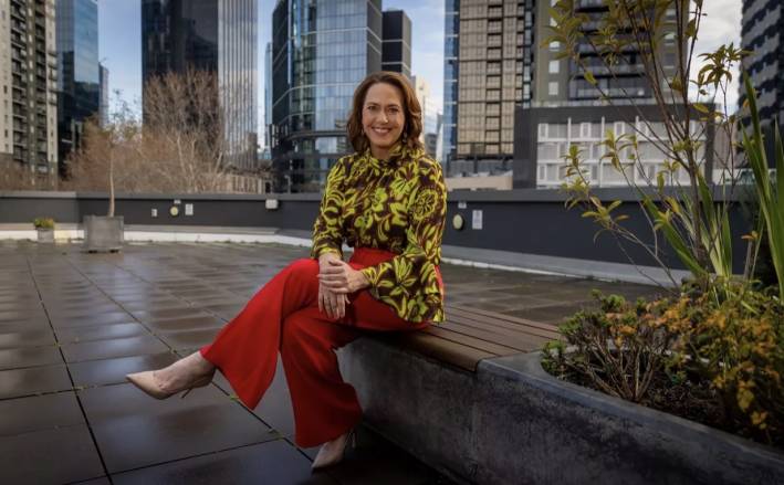 Lisa Millar sitting down on a stone wall outside some offices.