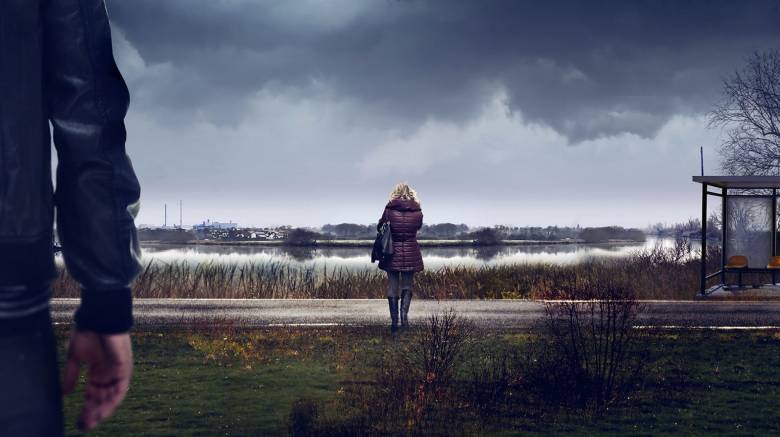 Key art for Sambre – Anatomy of a Crime. A unidentifiable person stands close to camera, facing towards the other person in the image. A woman stands a short distance away, by a roadside with her back to the camera. A bus shelter is in the corner of the scene. Grey clouds hang overhead.