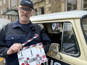 Greg Davies stands in front of a car holding a clapperboard for The Cleaner series three.