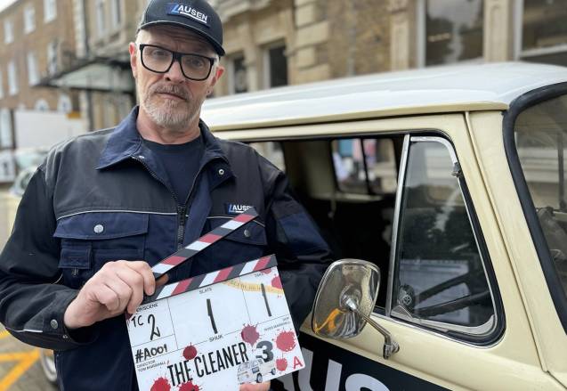 Greg Davies stands in front of a car holding a clapperboard for The Cleaner series three.