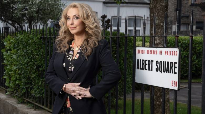 Tracey-Ann Oberman looking to camera and standing beside the Albert Square road sign